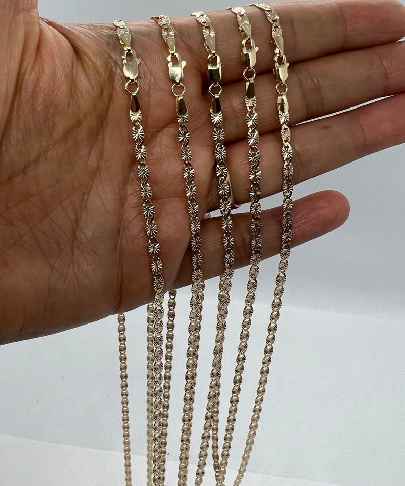 May include: Five gold chains with a diamond-cut design. The chains are arranged in a row, with the shortest chain at the top and the longest chain at the bottom.