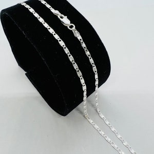 Puede incluir: Un collar de cadena de plata con un dise&ntilde;o de cadena de caja. La cadena est&aacute; en un expositor de terciopelo negro.