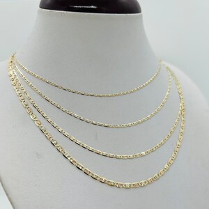 May include: Four gold-coloured chain necklaces of varying lengths displayed on a white mannequin bust. The chains have a flat, mariner link design. The necklaces are arranged to show different lengths and styles.