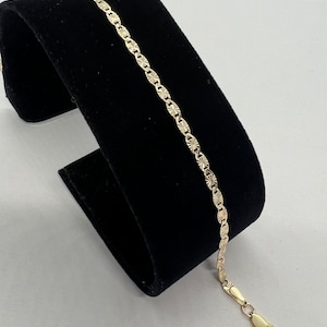 May include: A gold chain bracelet with a textured, diamond-shaped pattern. The bracelet has a lobster claw clasp.