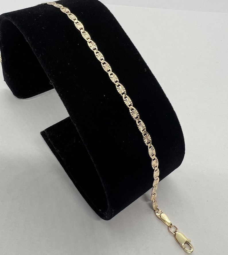 May include: A gold chain bracelet with a textured, diamond-shaped pattern. The bracelet has a lobster claw clasp.