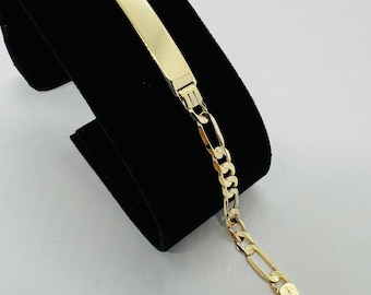 May include: A gold chain bracelet with a rectangular tag. The chain is a figaro style with alternating large and small links.