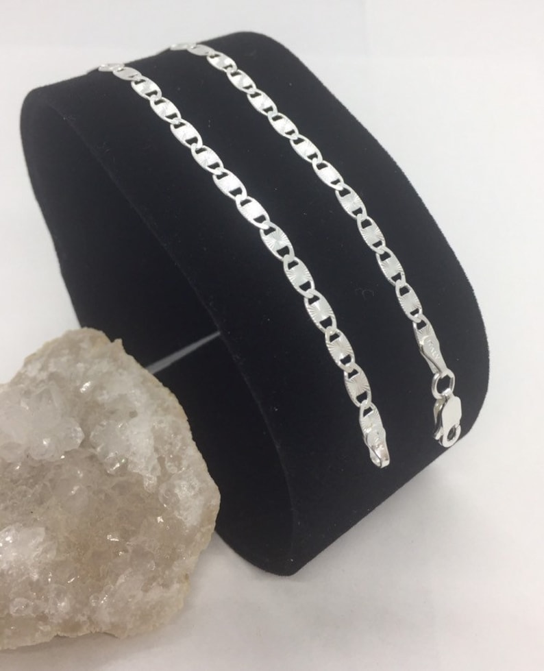 May include: A silver mariner chain necklace with a shiny finish. The chain is displayed on a black velvet stand.
