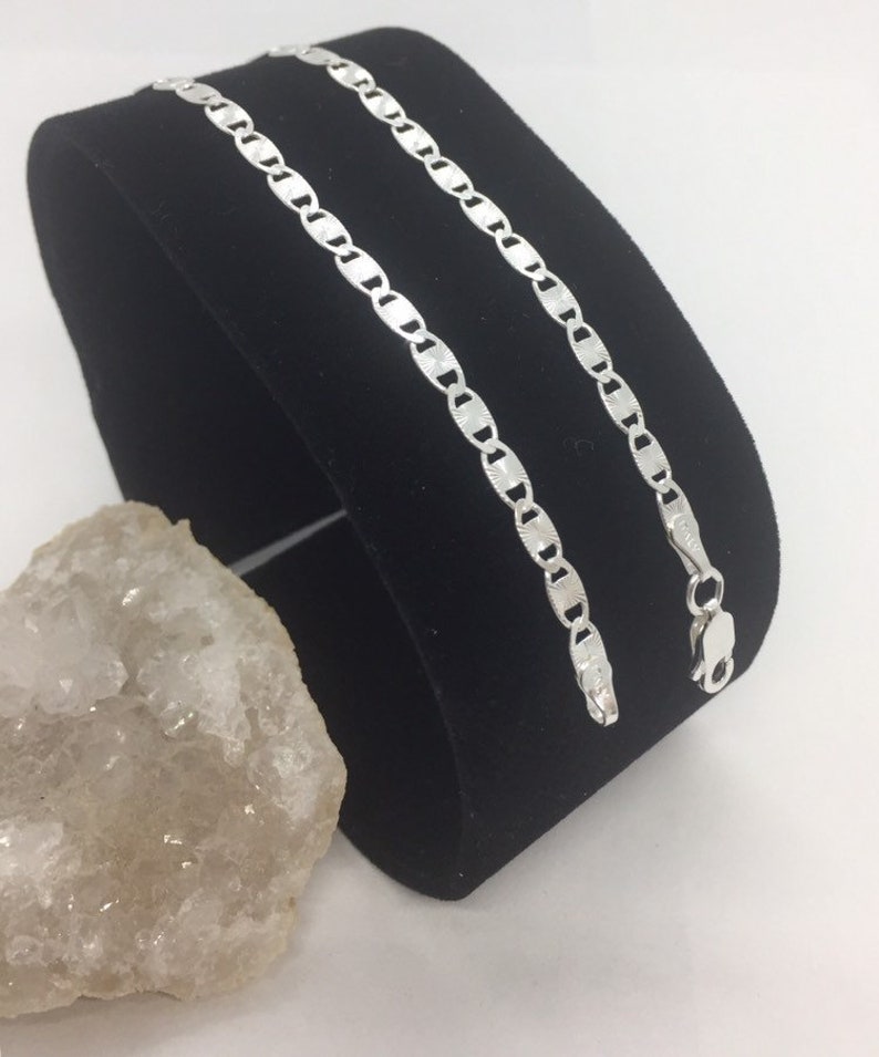 May include: A silver chain necklace with a mariner link design. The chain is displayed on a black velvet background.