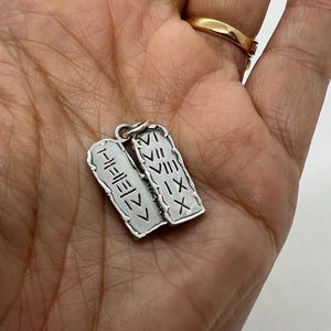 May include: Two silver pendants shaped like tablets with Roman numerals engraved on them. The pendants are connected by a silver ring.