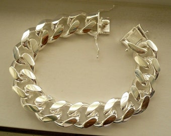 May include: A silver curb chain bracelet with a lobster clasp closure. The chain is thick and has a polished finish.