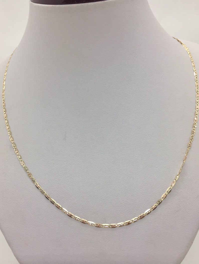 May include: A gold chain necklace with a delicate, patterned design. The chain is on a white display stand.