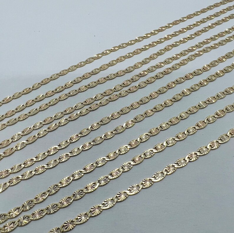 May include: A set of eight gold-toned chains with a diamond-shaped pattern. The chains are arranged in a staggered pattern, with the longest chain at the top and the shortest chain at the bottom.