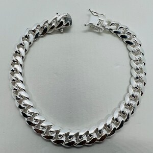 May include: A silver curb chain bracelet with a lobster clasp closure.