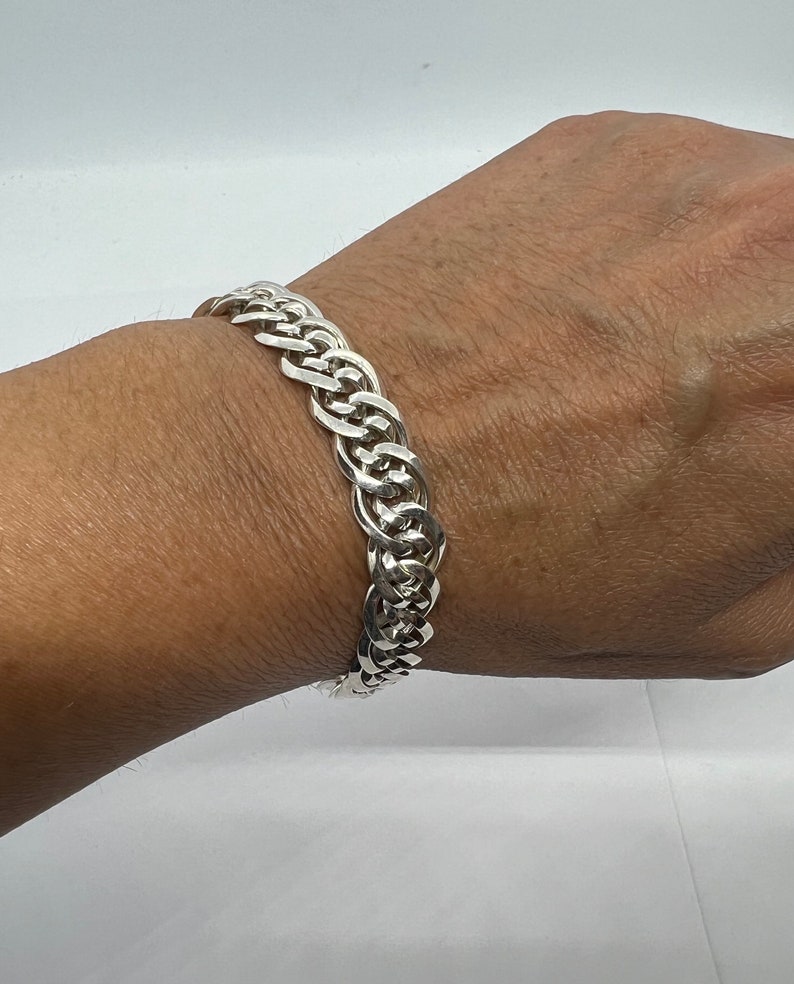 Op de afbeelding: Een zilveren kettingarmband met een dik, verweven ontwerp.