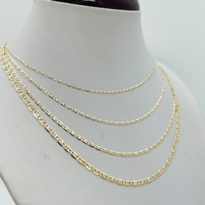 May include: Four gold-coloured mariner chain necklaces of varying thicknesses displayed on a white mannequin bust. The chains have a flat, oval link design, and are presented in a layered arrangement, showcasing the different sizes.
