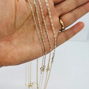 May include: A selection of gold-coloured chain necklaces in various styles and thicknesses. The chains are held against a light background, highlighting their different designs and clasps. The necklaces appear to be made of a shiny, metallic material.