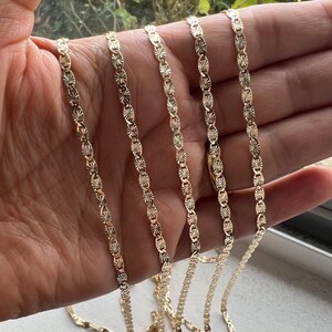 May include: Four gold chains with a diamond-shaped pattern. The chains are laid out in a row on a hand.