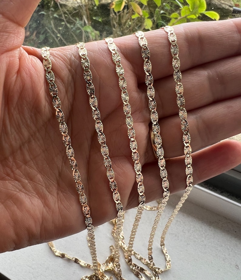 May include: Four gold chains with a diamond-shaped pattern. The chains are laid out in a row on a hand.