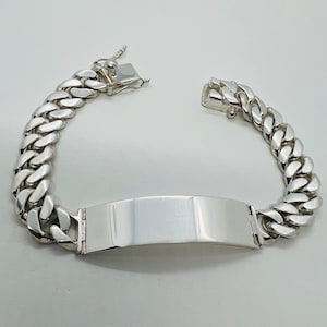 May include: A silver curb chain bracelet with a flat, rectangular tag. The tag is smooth and has a polished finish.