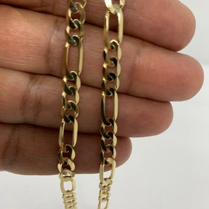 May include: A gold chain necklace with a figaro link pattern. The chain is shown folded in half, with the ends of the chain visible.