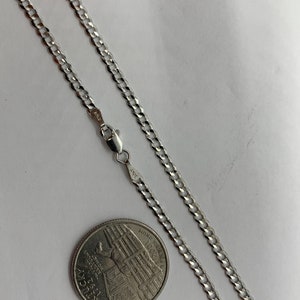 May include: A silver curb chain necklace with a lobster clasp. The chain is laid out on a white surface next to a US quarter.