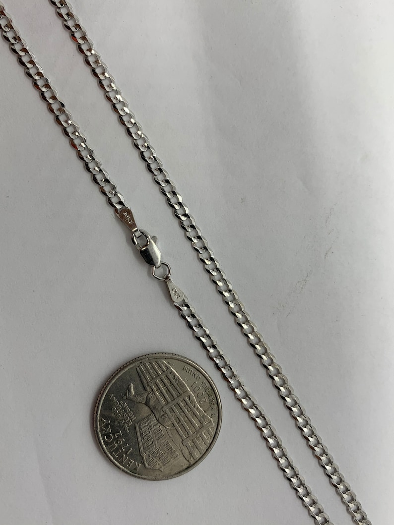 May include: A silver curb chain necklace with a lobster clasp. The chain is laid out on a white surface next to a US quarter.