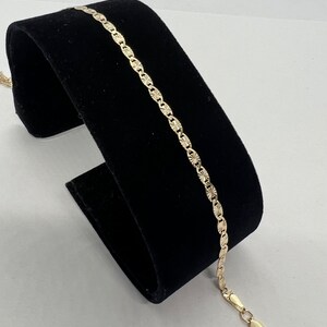 May include: A gold chain bracelet with a textured, diamond-shaped pattern. The bracelet has a lobster claw clasp.