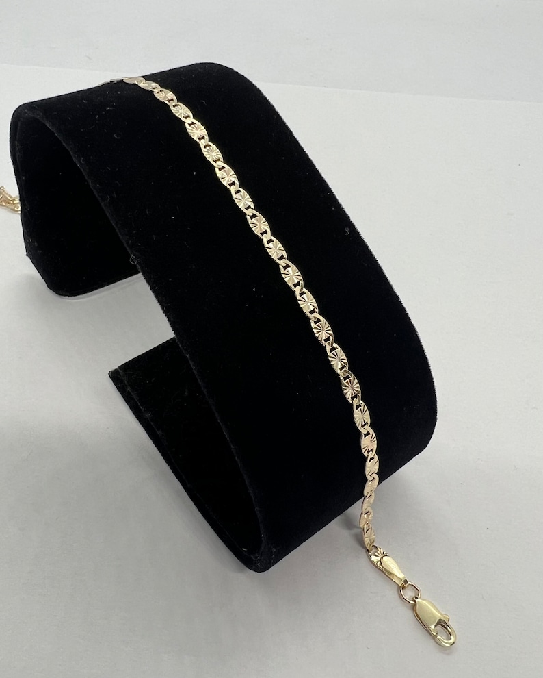 May include: A gold chain bracelet with a textured, diamond-shaped pattern. The bracelet has a lobster claw clasp.