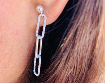 May include: Silver chain earrings with a small ball at the top and three oval links. The links are twisted and have a shiny finish.