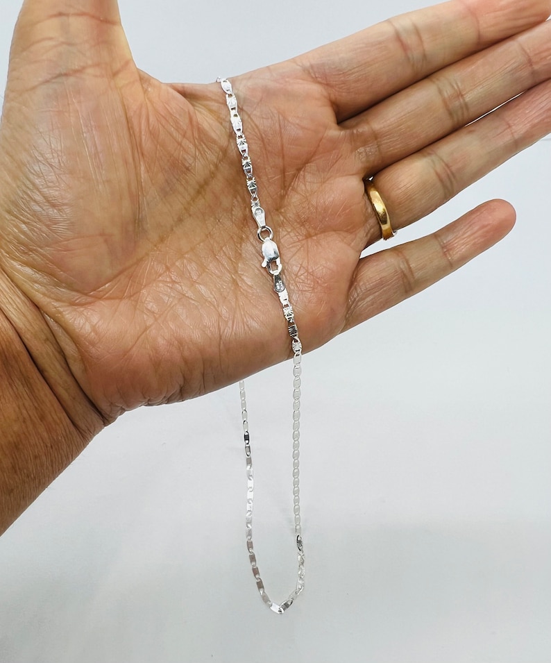 Puede incluir: Un collar de cadena de plata con un dise&ntilde;o de cadena de caja. La cadena est&aacute; en una mano, y el cierre es visible.