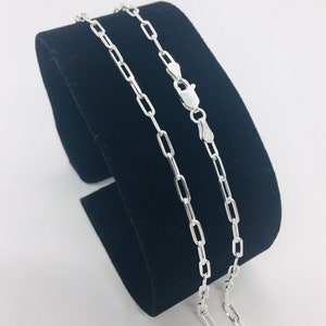 May include: A silver chain necklace with a box chain design. The chain is displayed on a black velvet stand.