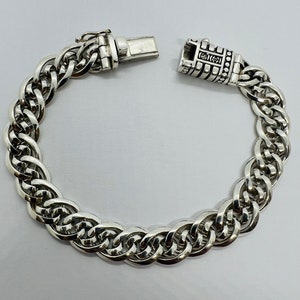 Op de afbeelding: Een zilveren kettingarmband met een gedetailleerde sluiting. De ketting is gemaakt van verweven schakels, waardoor een dikke en substanti&euml;le uitstraling ontstaat.