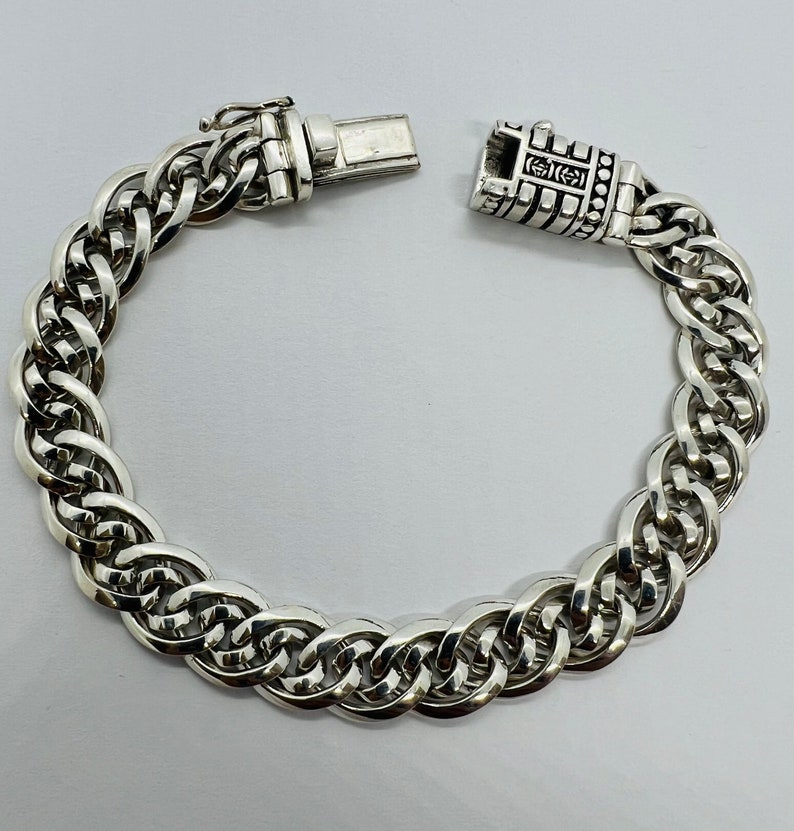 Op de afbeelding: Een zilveren kettingarmband met een gedetailleerde sluiting. De ketting is gemaakt van verweven schakels, waardoor een dikke en substanti&euml;le uitstraling ontstaat.