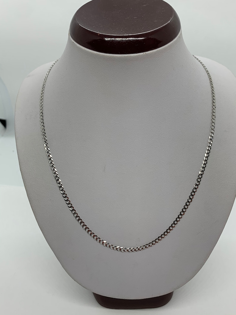 May include: A silver curb chain necklace on a white display stand.