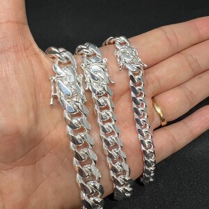 May include: Three silver Cuban link chains of different sizes, displayed on a hand.