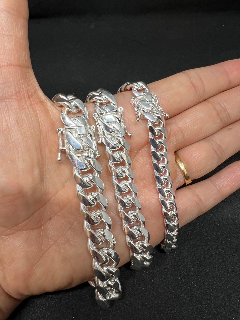 May include: Three silver Cuban link chains of different sizes, displayed on a hand.