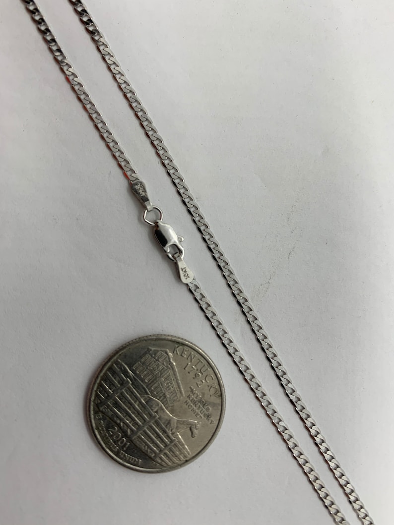 May include: A silver curb chain necklace with a lobster clasp. The chain is laid out on a white surface next to a US quarter.