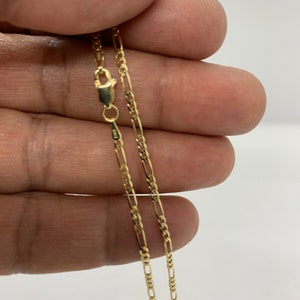 May include: A gold chain necklace with a lobster clasp. The chain is a figaro style with alternating links.