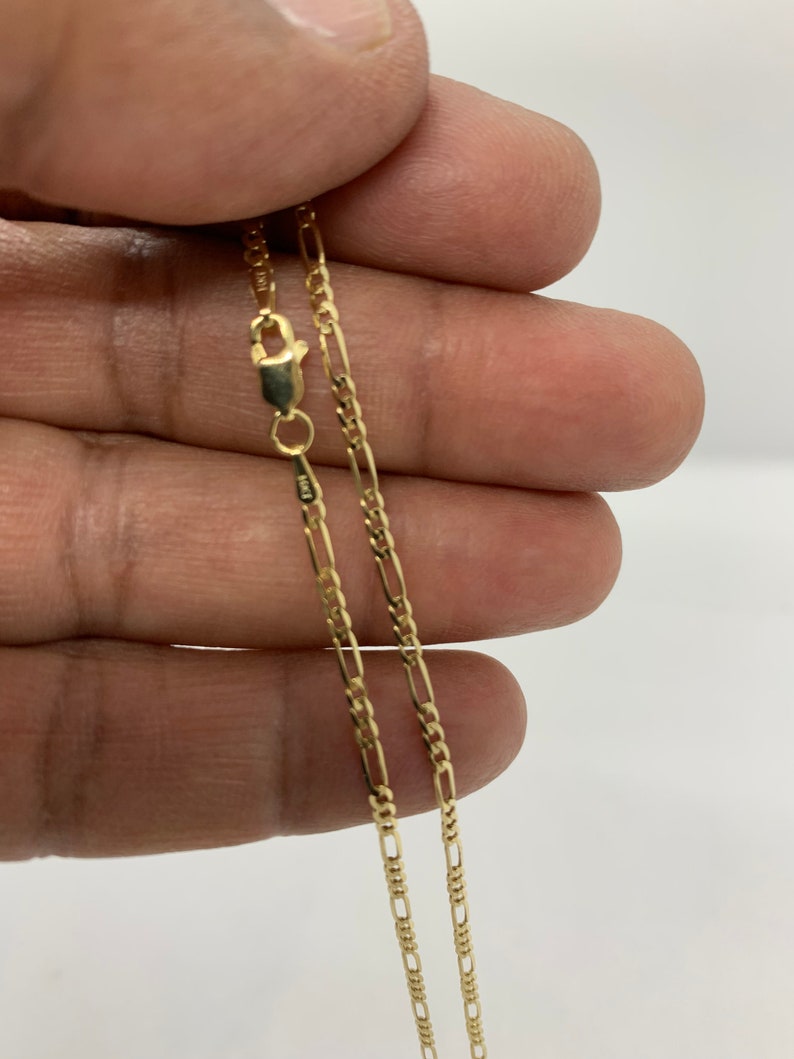 May include: A gold chain necklace with a lobster clasp. The chain is a figaro style with alternating links.
