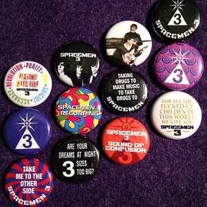 Puede incluir: Una colección de 12 botones de la banda Spacemen 3. Los botones son redondos y presentan varios diseños, incluidos logotipos de la banda, portadas de álbumes y letras de canciones. Los botones son todos en blanco y negro con letras doradas.
