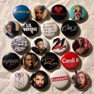 May include: A collection of 16 round button pins featuring various hip hop artists and song titles. The pins are black, white, red, blue, and gray with white text. Some of the pins feature images of the artists, while others feature text only. The text on the pins includes "Cardi B", "Lil Wayne", "Drake", "XXXTENTACION", "Savage", "Put it all in a plastic bag", "Esskeetit", "If you're reading this it's too late", and "Take Care".