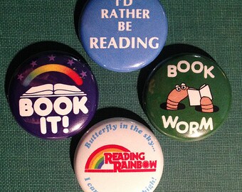 Könnte beinhalten: Vier bunte Anstecknadeln mit Buchmotiven. Die erste Nadel ist blau mit weißem Text, der "I'd Rather Be Reading" lautet. Die zweite Nadel ist lila mit einem Regenbogen, einem Buch und weißem Text, der "Book It!" lautet. Die dritte Nadel ist grün mit einem weißen Wurm, der ein Buch liest, und dem Text "Book Worm". Die vierte Nadel ist weiß mit einem Regenbogen und dem Text "Butterfly in the sky... Reading Rainbow I can go twice as high!"