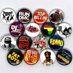 Op de afbeelding: Een verzameling van 15 ronde knoppen met verschillende hiphop-artiesten en -groepen, waaronder Run DMC, Salt-N-Pepa, Biz Markie en UTFO. De knoppen zijn zwart, rood, wit en geel.