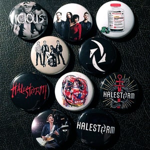 May include: Nine button pins featuring a variety of designs, including a band logo, a skull, a bottle of pills, and a band's name. The pins are all black and white with red accents.