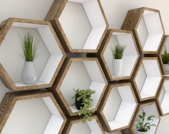 May include: A set of hexagonal shelves made of wood with white interiors. The shelves are arranged in a honeycomb pattern and are decorated with potted plants.