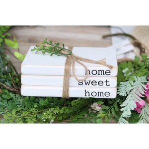 May include: Three white books stacked on top of each other with twine tied around them. The books are decorated with the words "home sweet home" in black lettering.