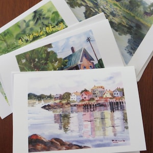 May include: Four watercolor paintings on white card stock. The top painting shows a green landscape with a pond and yellow flowers. The second painting shows a house with a green roof and a blue sky. The third painting shows a waterfront scene with a row of houses and a sailboat. The bottom painting shows a waterfront scene with a row of houses and a sailboat.