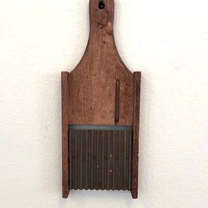 May include: A vintage wooden washboard with a dark brown finish. The washboard features a grooved metal scrubbing surface and a handle with a hole for hanging. The design is simple and functional, showcasing a rustic aesthetic.