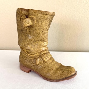 May include: A small, decorative boot figurine in a speckled, golden-brown color. The boot features a buckle detail and a low heel. The boot is approximately 6 inches tall.