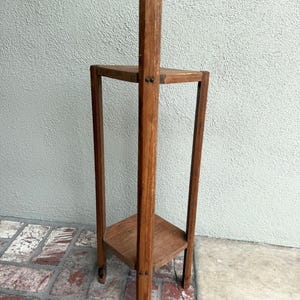 May include: A three-tiered, wooden plant stand with a natural finish. The stand has a central vertical support and three square shelves. The stand is approximately 76 cm tall and 30 cm wide.