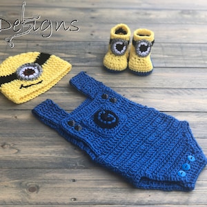 May include: A crocheted Minion costume set for a baby, including a yellow hat with a black strap and a single eye, blue overalls with a black G on the front, and yellow booties with a black eye on each.