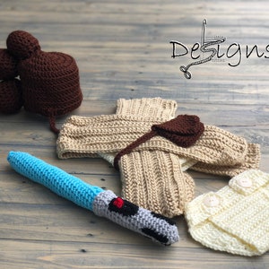 May include: A crocheted baby outfit inspired by Star Wars, featuring a brown hat with a bun, a beige robe, a brown pouch, a blue lightsaber, and a white diaper.
