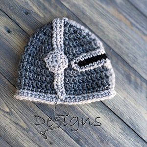 Puede incluir: Un casco de crochet gris y marr&oacute;n con una visera negra. El casco est&aacute; sobre una superficie de madera con el texto "Little Stitches Designs" en blanco.
