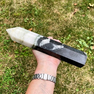 May include: A large, white, green, and black crystal point, also known as a wand, with a pointed tip and a hexagonal base.